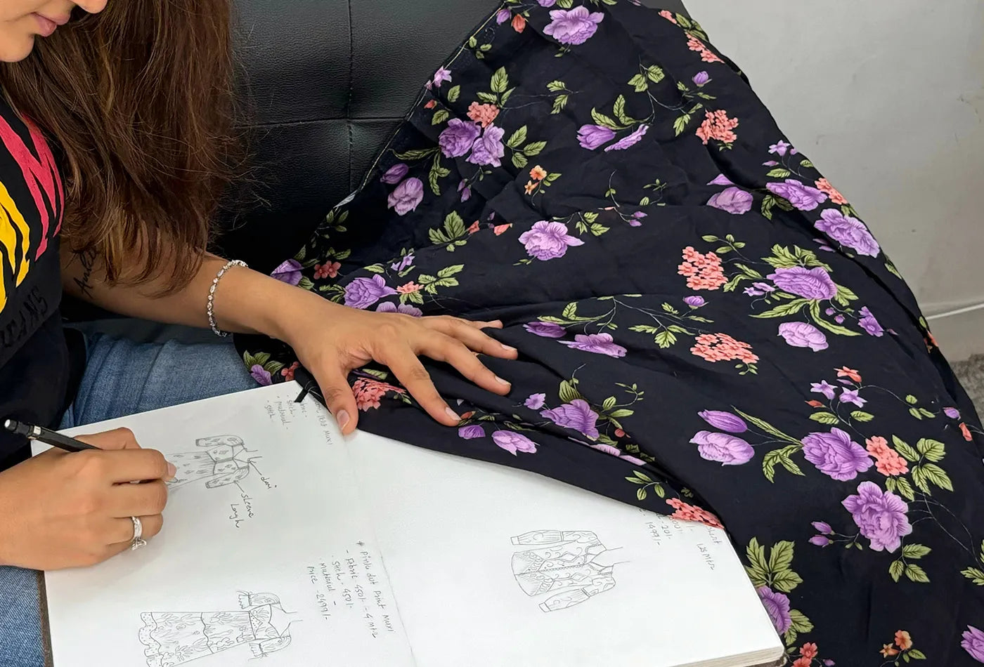 Anrobee owner creating a fresh dress design, sketching patterns inspired by black floral fabric.