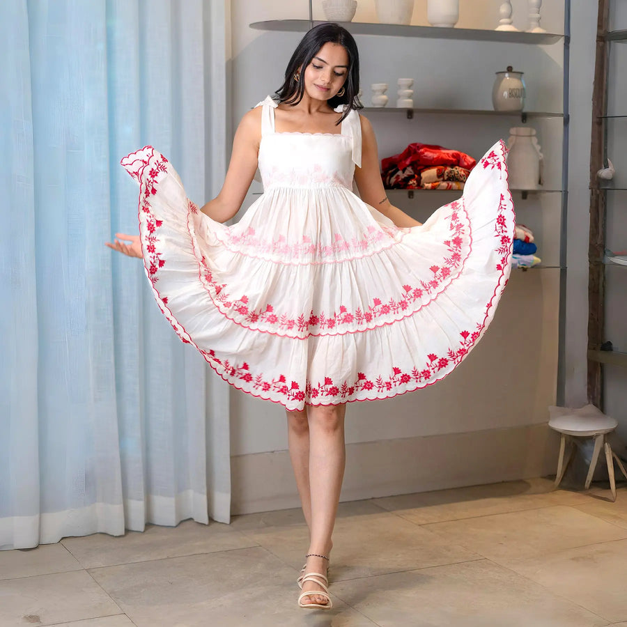 Flared silhouette of a white one piece frock dress with pink embroidery and feminine tiers