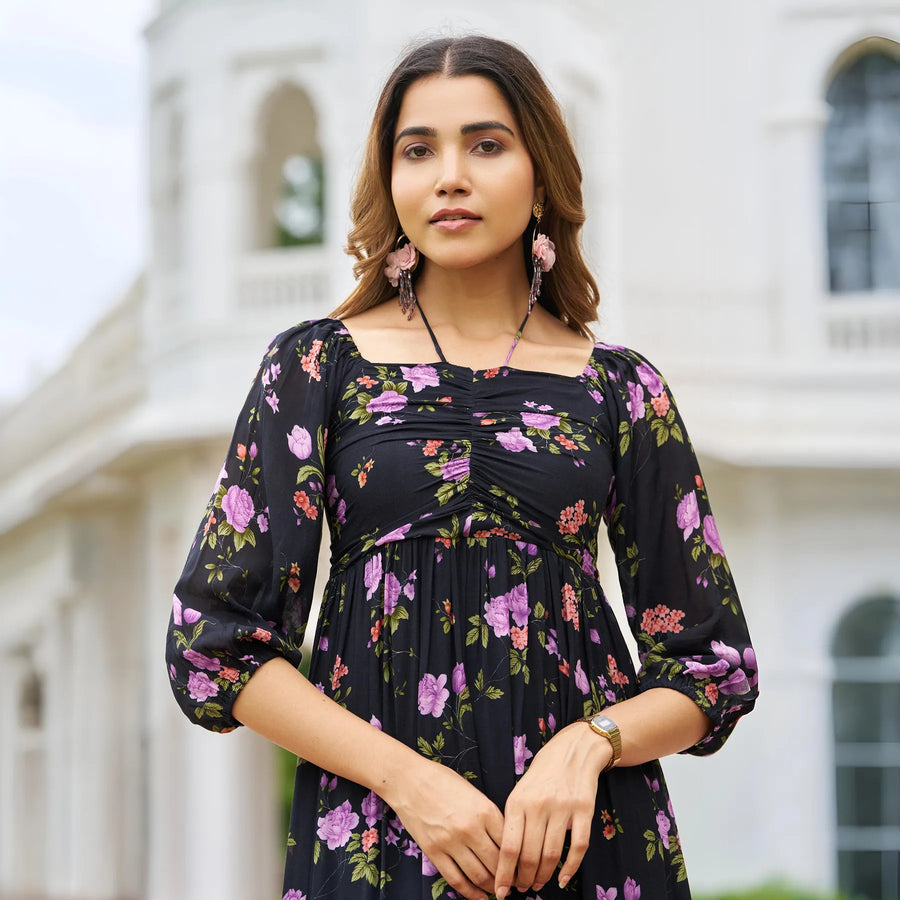 Close-up of black floral midi dress with ruched neckline and sleeves, woman posing confidently.