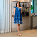 Front pose showing a chic knee length one piece dress with one-shoulder neckline and embroidered hem