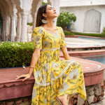 Close-up sitting pose of Marigold Aura yellow midi dresses – ideal for Haldi functions with festive floral charm.