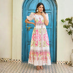 Model wearing a white maxi dress with heritage-inspired pink and olive motifs, standing in a front pose.