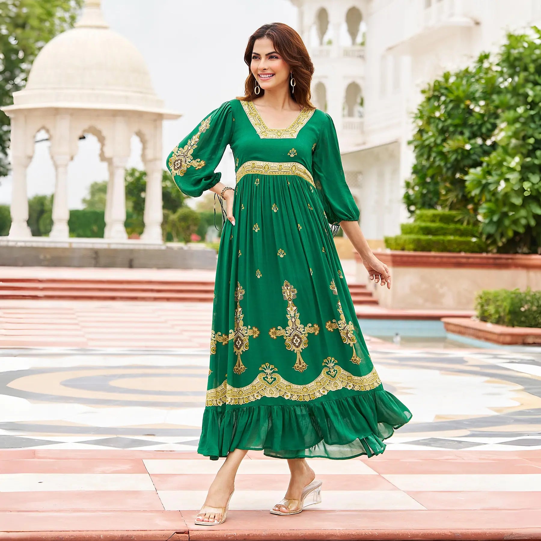Walking side pose in an emerald green a line maxi dress with gold detailing, styled for festivals and cultural events.
