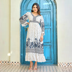 Model wearing a white maxi dress for women with deep navy floral border print, V-neckline, and 3/4 sleeves, standing in a front pose.