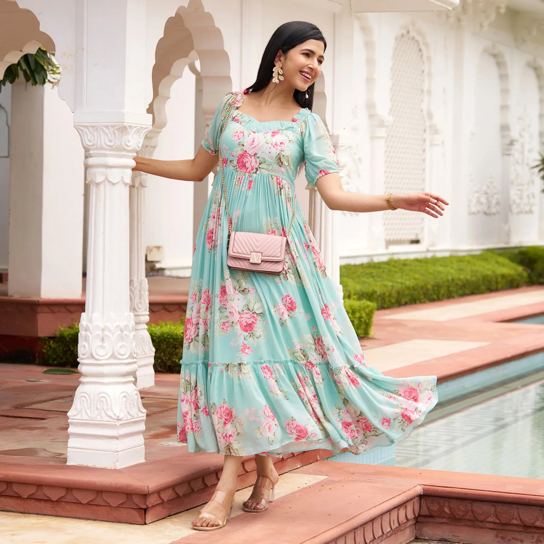 Woman walking gracefully in Mint Bloom long floral beach dress, styled with pink bag, perfect for vacation and resort wear.