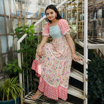 Sitting pose on staircase in a floral maxi one-piece, styled for festive occasions.