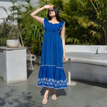 Outdoor shot of a summer maxi dress in vibrant blue, model shading eyes from sunlight.
