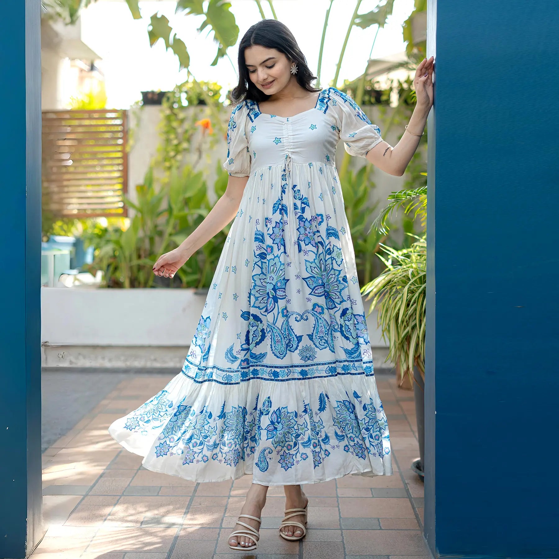Model twirling in a blue floral maxi dress outdoors, styled for vacations and breezy summer outings.