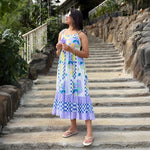 Woman in Sleeveless midi dress for walking on stone steps outdoors, holding a flower.