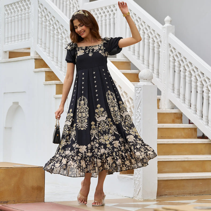 Elegant woman posing in a black one piece dress with gold motifs and a mini handbag