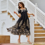 Model in black A-line midi dress resting her arm on a pillar, smiling softly